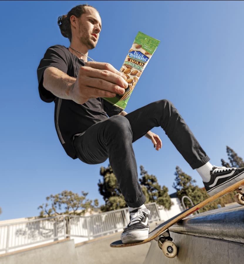 Man skateboarding while holding 1.5oz tube of Bold Wasabi & Soy Sauce almonds.